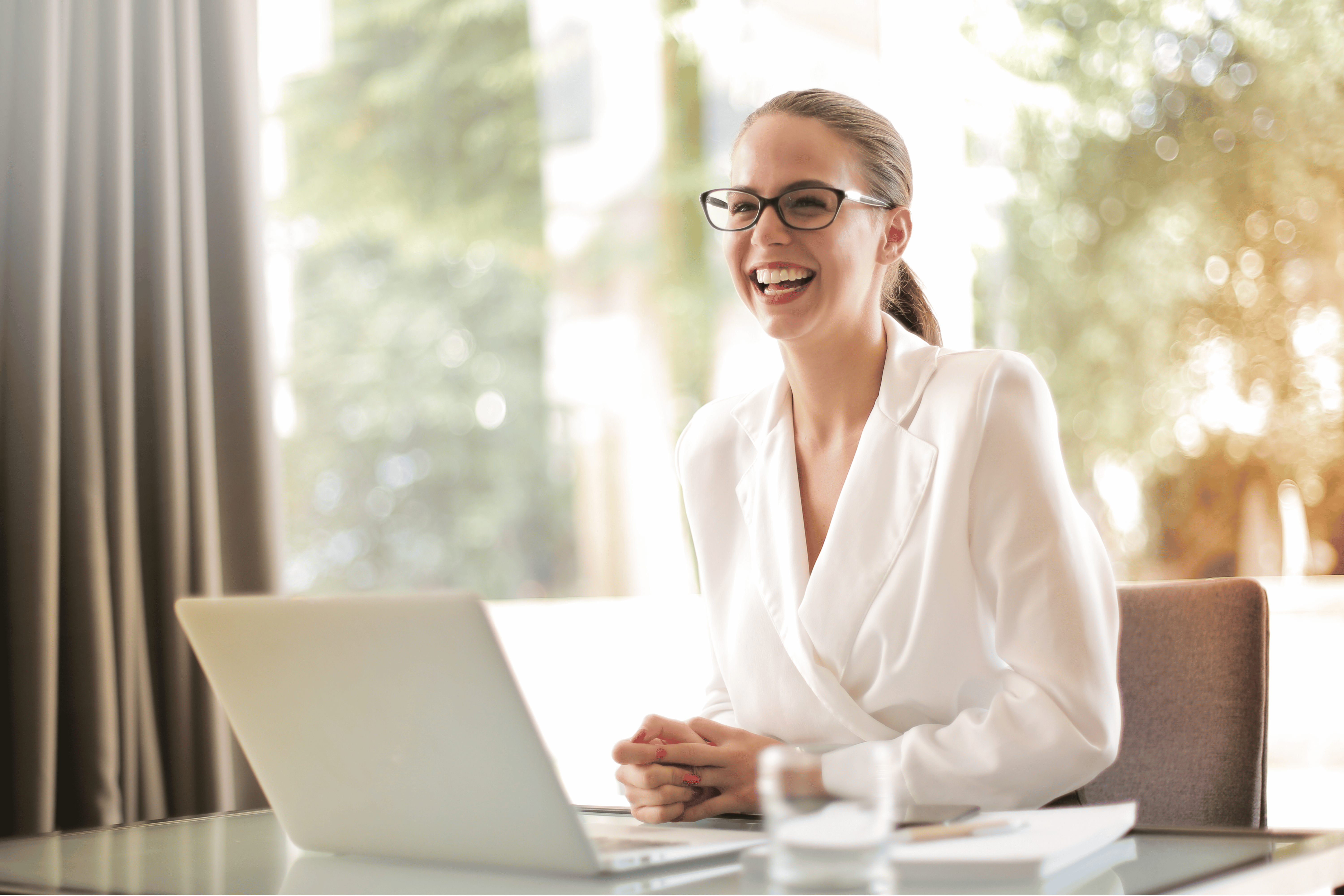 Image: A confident and empowered woman in a white blouse, smiling, symbolizing the positive and impactful outcomes of entrepreneur coaching.